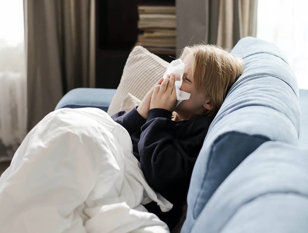 Ein Kind liegt krank auf dem Sofa und putzt sich die Nase